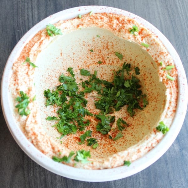 Creamy hummus in a white bowl, garnished with paprika and fresh parsley.