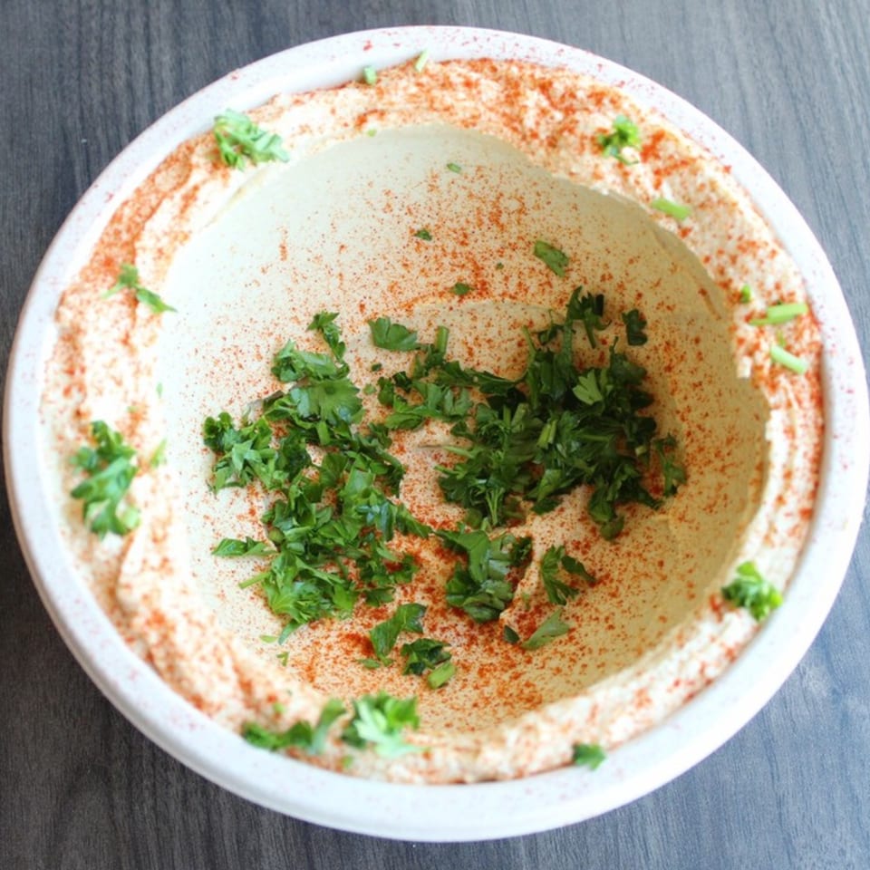Creamy hummus in a white bowl, garnished with paprika and fresh parsley.