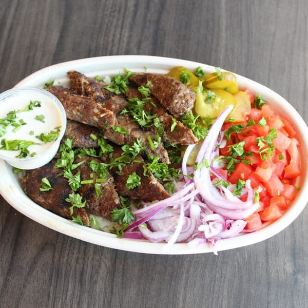 Baba Dari Mediterranean Grill's kofta kebab plate with rice, tomatoes, onions, pickles, and a side of sauce.