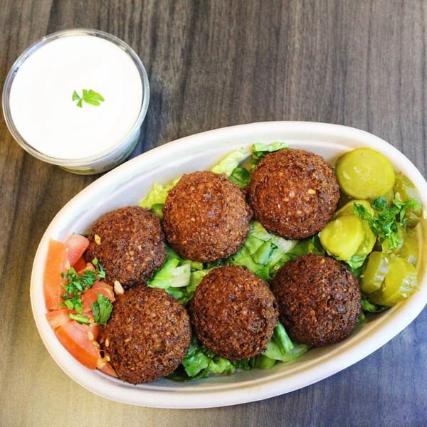 A Baba Dari Mediterranean Grill falafel plate with lettuce, tomatoes, pickles, and a side of white sauce.