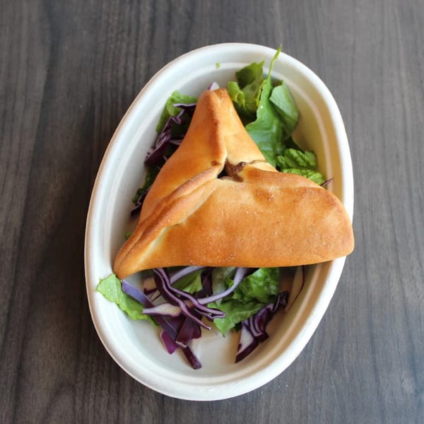 A golden-brown triangular pastry, likely a fatayer, rests on a bed of fresh green and purple lettuce.