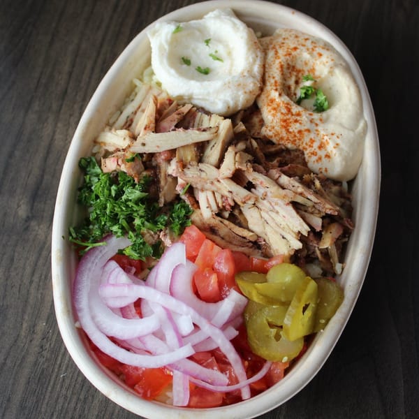 Mediterranean chicken shawarma bowl with hummus, garlic sauce, tomatoes, onions, pickles, and parsley.