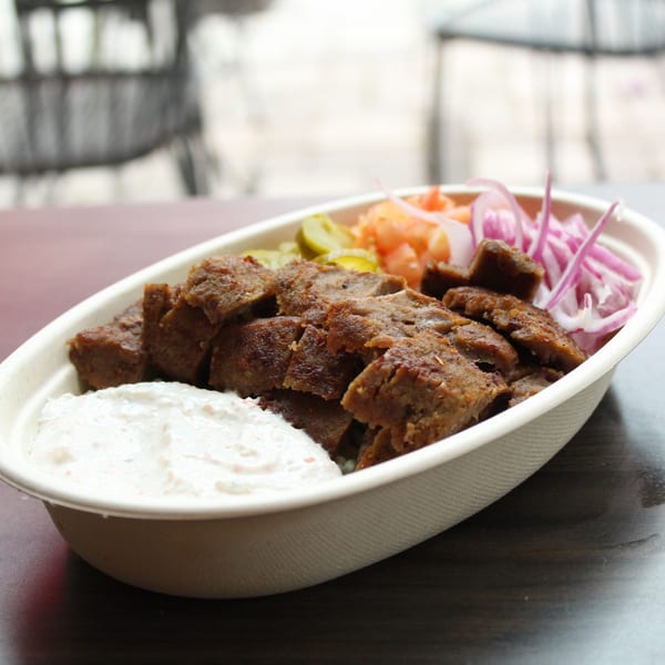 Mediterranean gyro bowl with sliced meat, white sauce, pickled onions, and cucumbers.