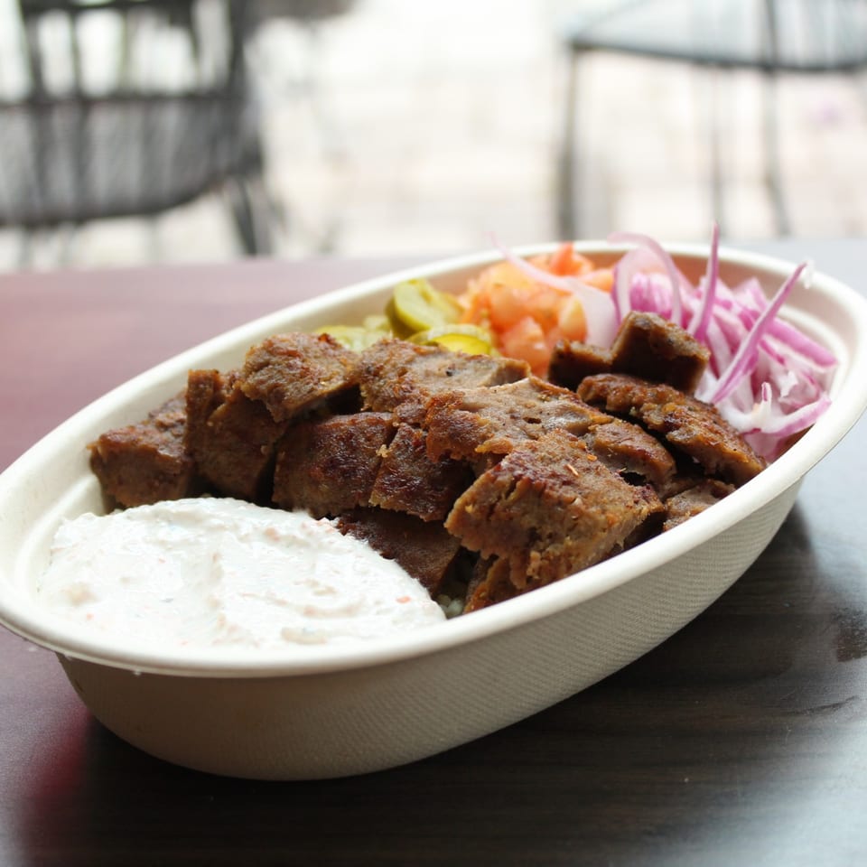 Mediterranean gyro bowl with sliced meat, white sauce, pickled onions, and cucumbers.