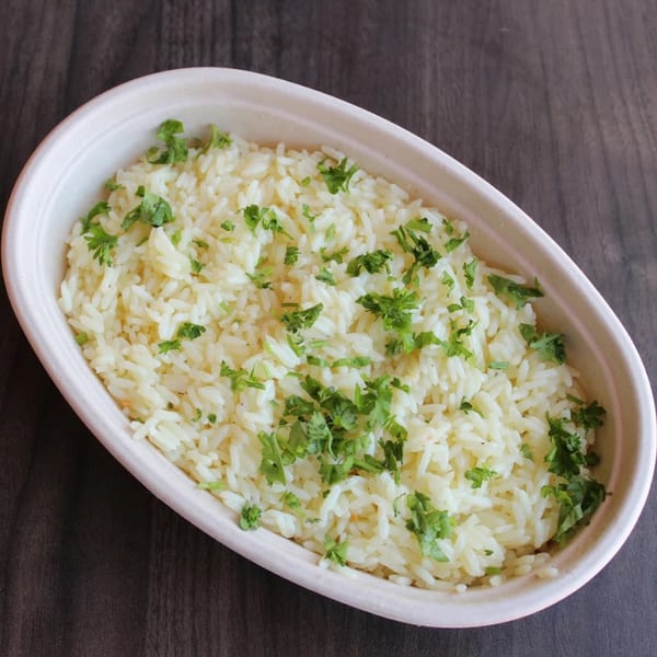 Fluffy white rice topped with fresh green parsley in an oval bowl on a dark wooden surface.
